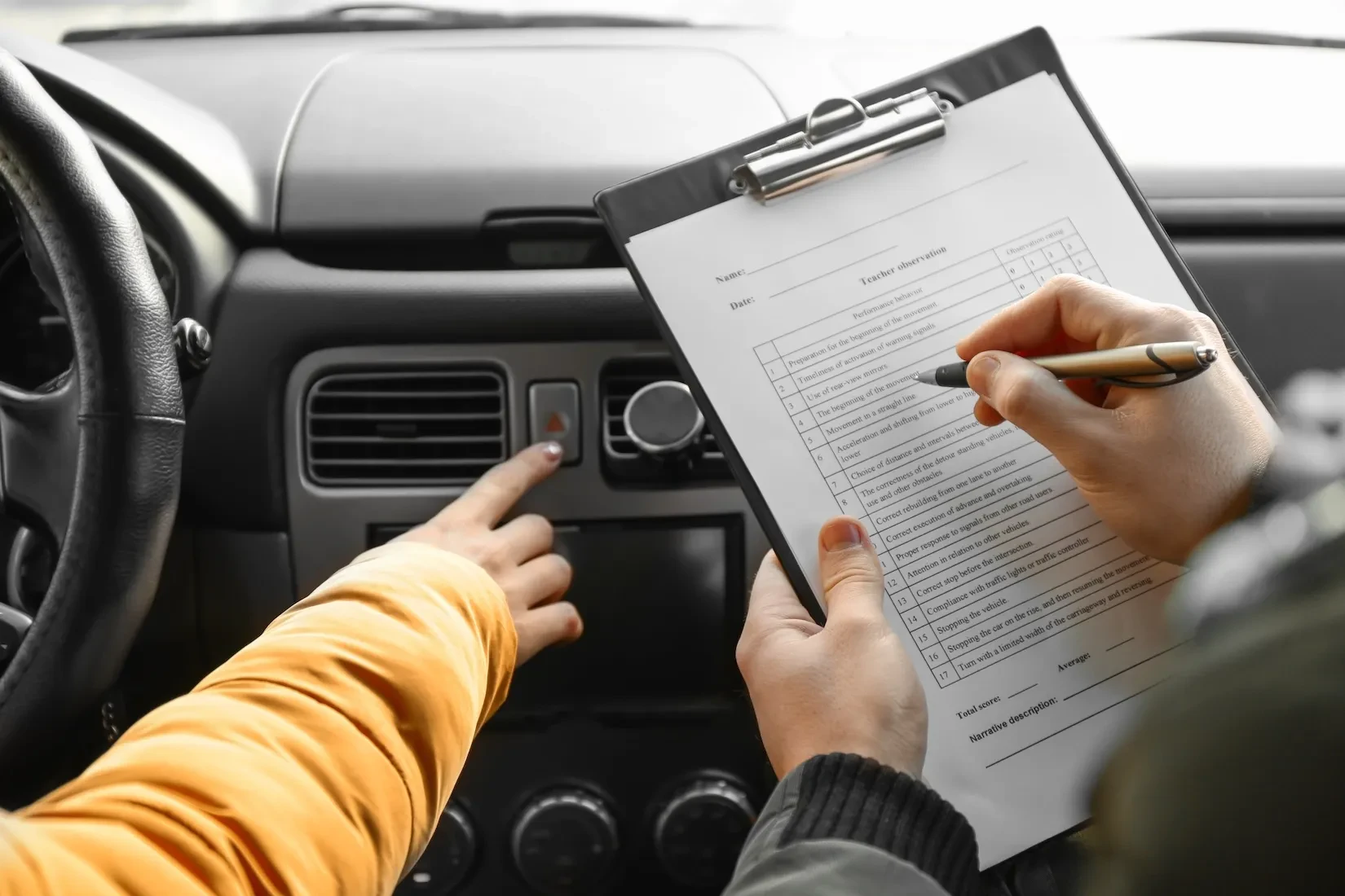 Fahrer im Auto drückt den Warnblinkerknopf, während eine andere Person auf einem Klemmbrett eine Fahrbeobachtungsbewertung ausfüllt.