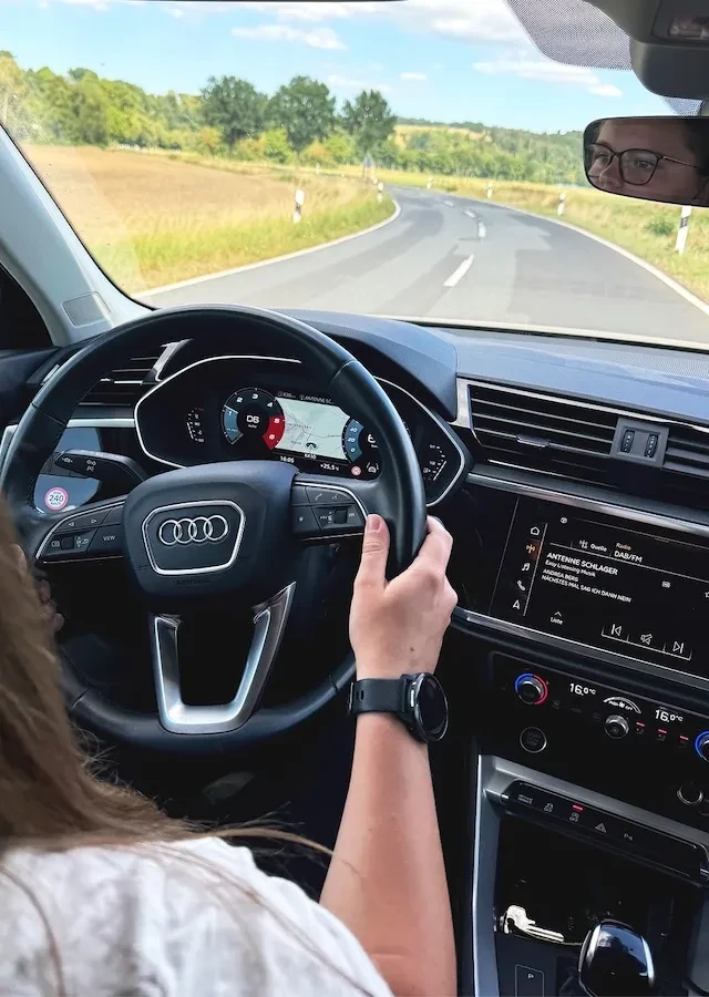 Person fährt ein Audi-Auto auf einer kurvigen Landstraße mit Blick auf das Lenkrad und das digitale Armaturenbrett.